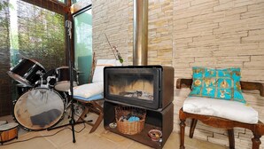 A cozy room with a stone wall, a fireplace, a drum set, and a chair with a patterned cushion.