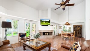 A spacious living room with a fireplace, a ceiling fan, and a television mounted above it. - Santa Rosa Cove #61 - 3 bedrooms, 3.5 Baths (La Quinta)
