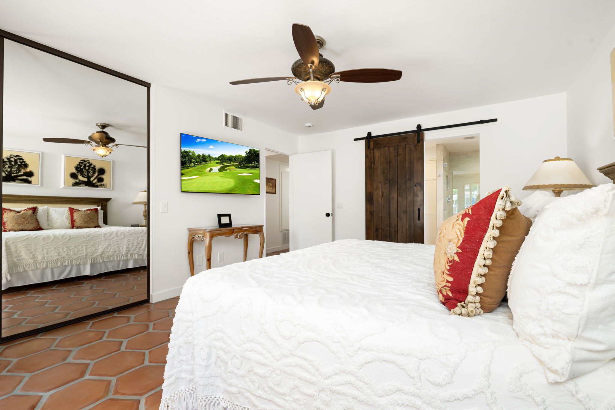 A bedroom with a large bed, a ceiling fan, a TV, and a sliding door.