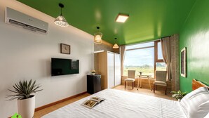 A modern hotel room with a large bed, a flat-screen TV, a potted plant, and a view of the outdoors. - Room in House - Trang An Ao Dai Homestay - Triple Room With Field View - Bich Dong Room (Hoa Lu)