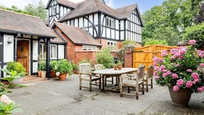 Ein Haus im Tudor-Stil mit Garten und einer Terrasse, auf der ein Holztisch und Stühle stehen.