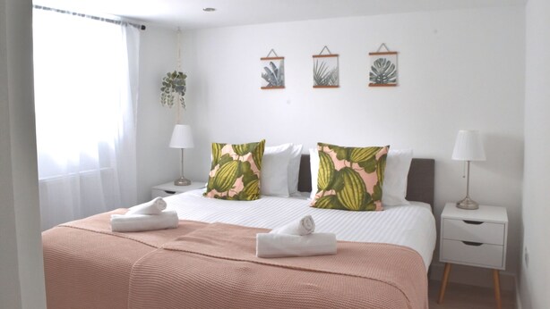 A hotel room with a neatly made bed, a bedside table with a lamp, and three framed wall art pieces above the bed. - New Flat near Luton Airport *FREE Parking* (Luton)