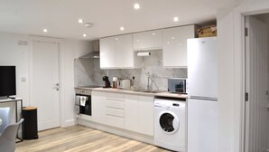 A modern kitchen with white cabinetry, a built-in oven, a washing machine, and a microwave. - New Flat near Luton Airport *FREE Parking* (Luton)