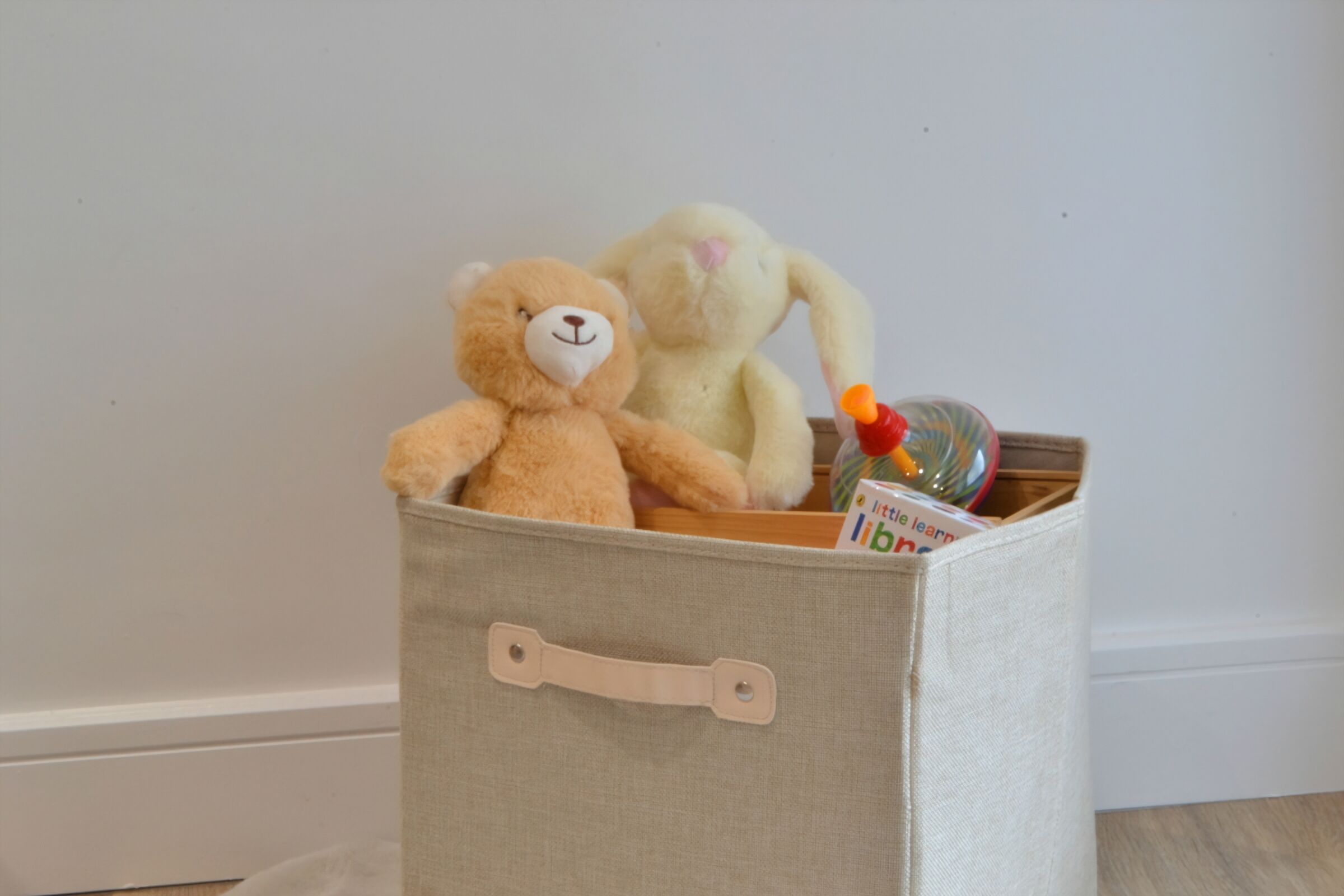 Une boîte de rangement avec une poignée, contenant un ours en peluche marron et un lapin en peluche blanc.