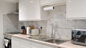 A modern kitchen with white cabinets, a marble backsplash, a stainless steel sink, and a built-in oven. - New Flat near Luton Airport *FREE Parking* (Luton)