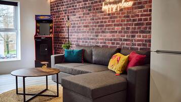 A cozy living area with a gray sectional sofa, a small round table, and a neon sign on the brick wall.