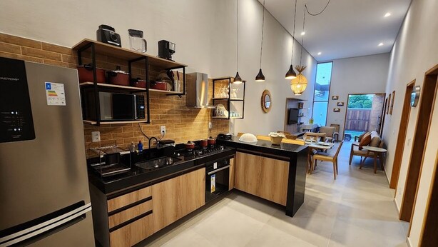 Een moderne keuken met een roestvrijstalen koelkast, houten kastjes, een zwart aanrecht en een eethoek met een tafel en stoelen.