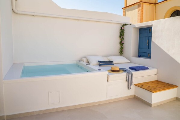 A modern bathroom with a built-in bathtub, a small wooden bench, and a window with blue shutters.