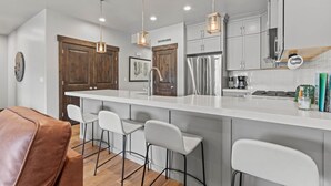 A modern kitchen with a central island, bar stools, stainless steel appliances, and pendant lighting. - Moose Mgmt at Black Rock 14442: Fully Equipped Kitchen-Pvt Hot Tub-Dogs Welcome (Park City)