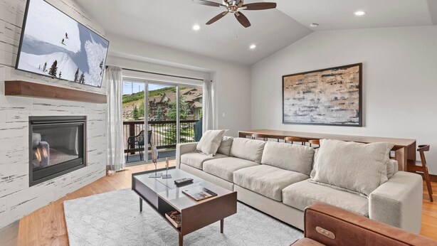 A modern living room with a fireplace, a large sofa, a coffee table, and a ceiling fan. - Moose Mgmt at Black Rock 14442: Fully Equipped Kitchen-Pvt Hot Tub-Dogs Welcome (Park City)