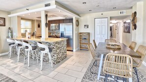 A modern kitchen with a central island, bar stools, and a dining area with wicker chairs.