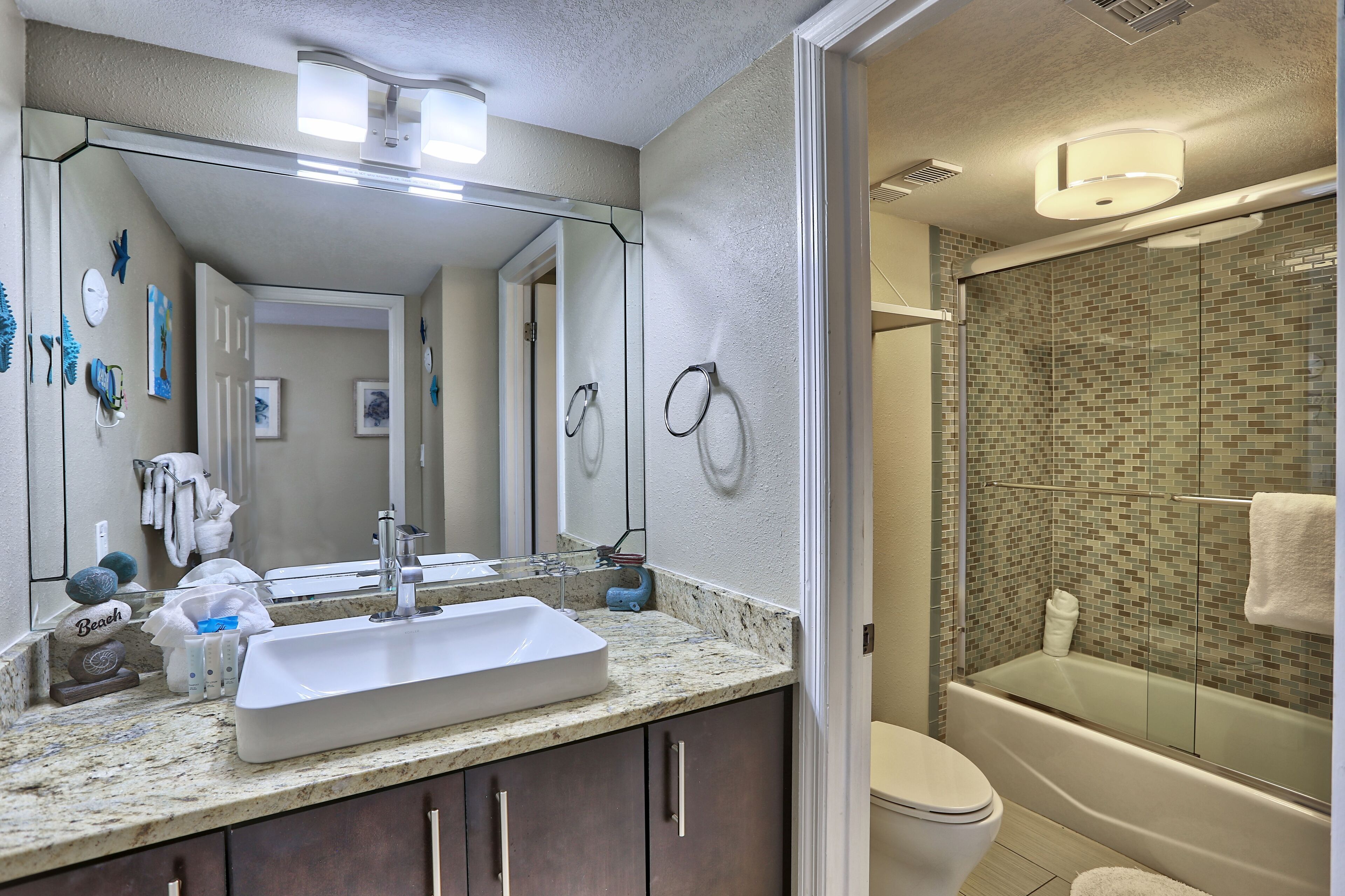 A bathroom with a large mirror, a sink, a toilet, and a glass-enclosed shower.