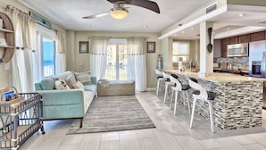 A spacious living area with a sofa, a coffee table, and a kitchen area with a bar and seating.