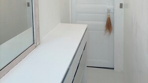 Une pièce blanche avec un grand miroir, une porte blanche et un luminaire placé au-dessus de la porte.