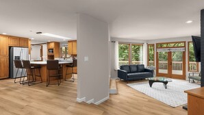 Une cuisine moderne avec des meubles en bois, un îlot central doté de tabourets de bar et un coin repas comprenant un canapé noir et une table basse.