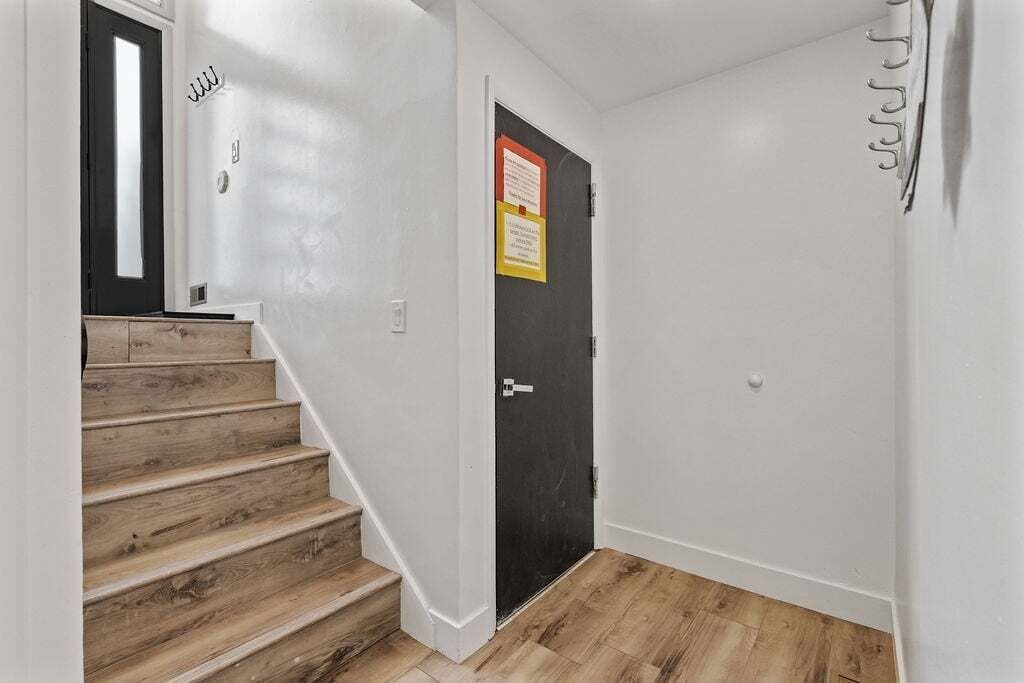 A staircase leading to a black door with a red and yellow sign, white walls, and wooden flooring.