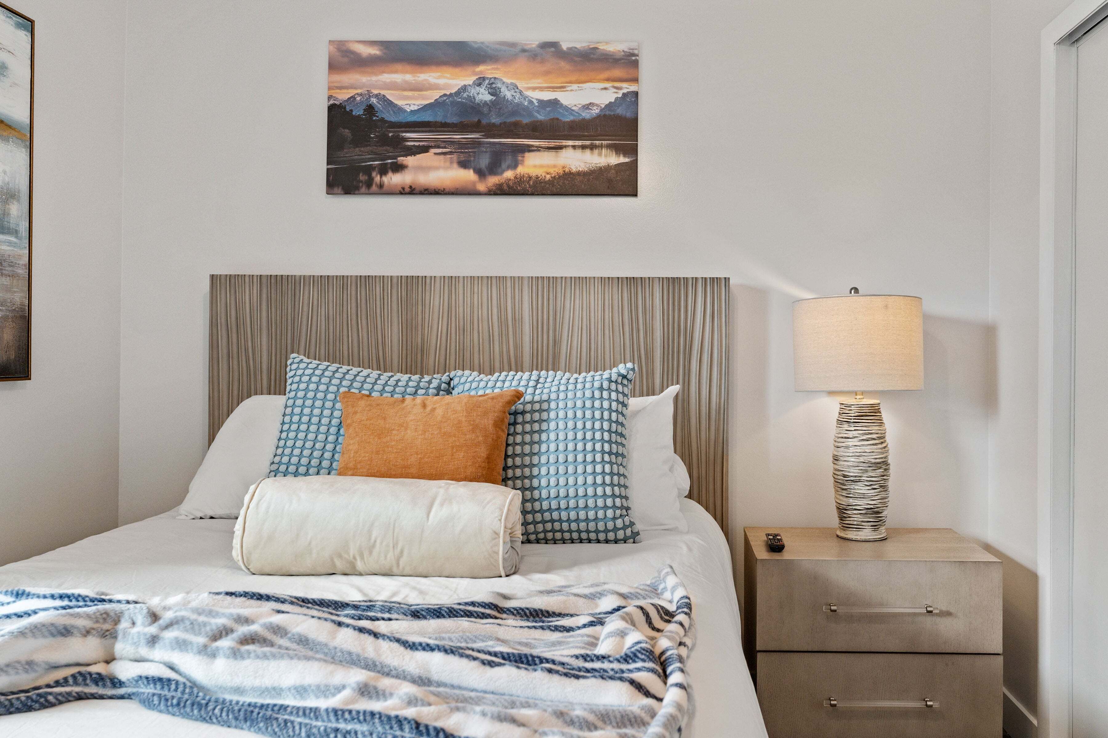 Un lit bien fait, agrémenté d’oreillers à motifs, une lampe de chevet et une commode.