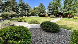 A well-maintained garden with a variety of shrubs and trees, a clear pathway leading to a building, and a gravel area in the foreground.