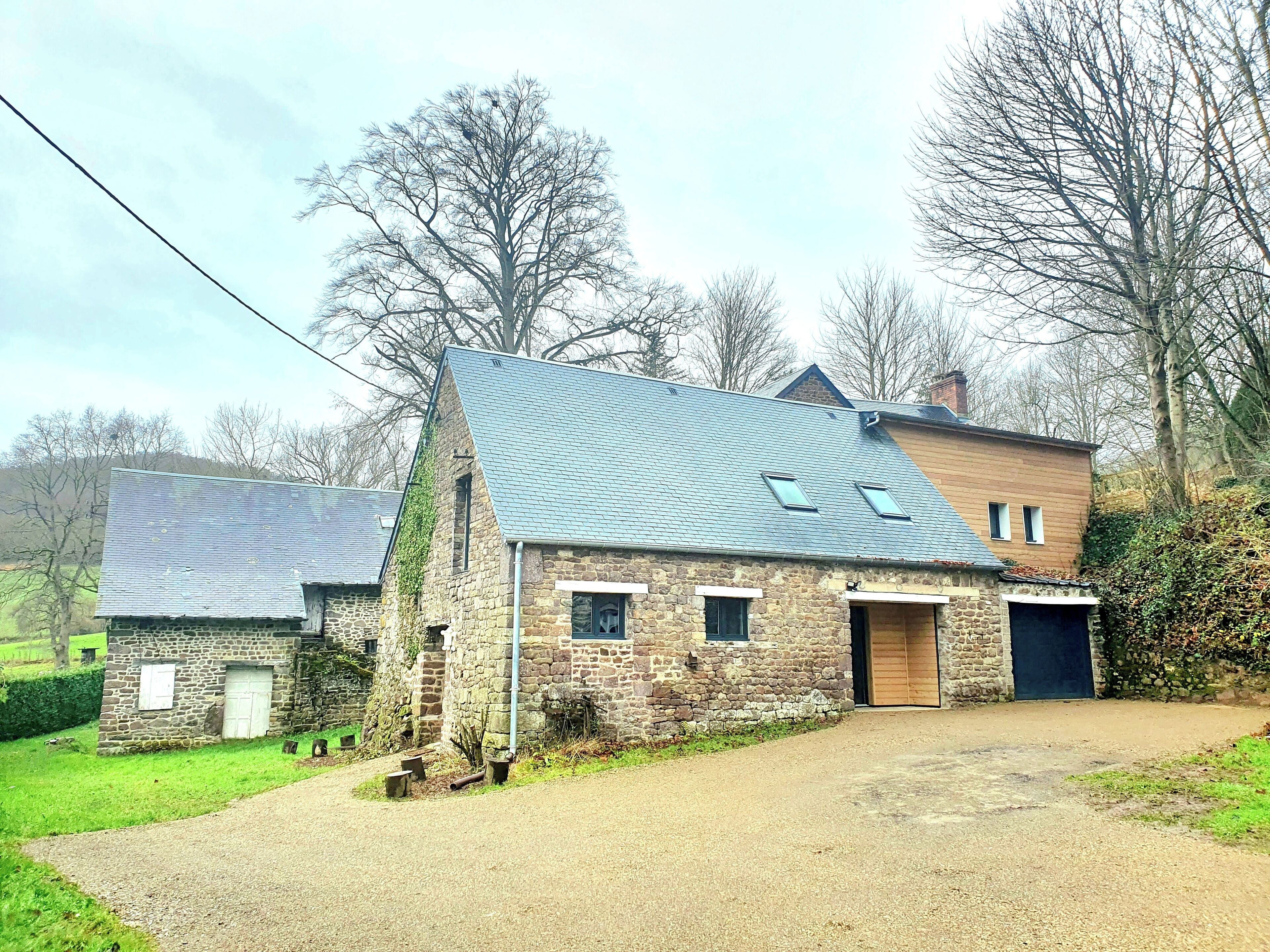 Une ferme en pierre avec un toit en pente, une porte en bois et une allée gravillonnée.