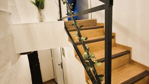 Una escalera de madera con barandilla de metal negro que conduce a un cuarto con una puerta blanca y una planta pequeña en el rellano.