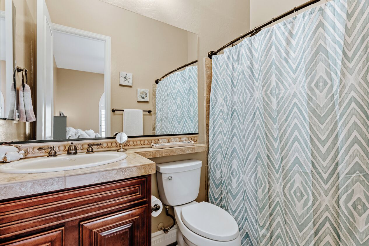 Un baño con lavamanos doble, inodoro y cortina de ducha con estampado geométrico.