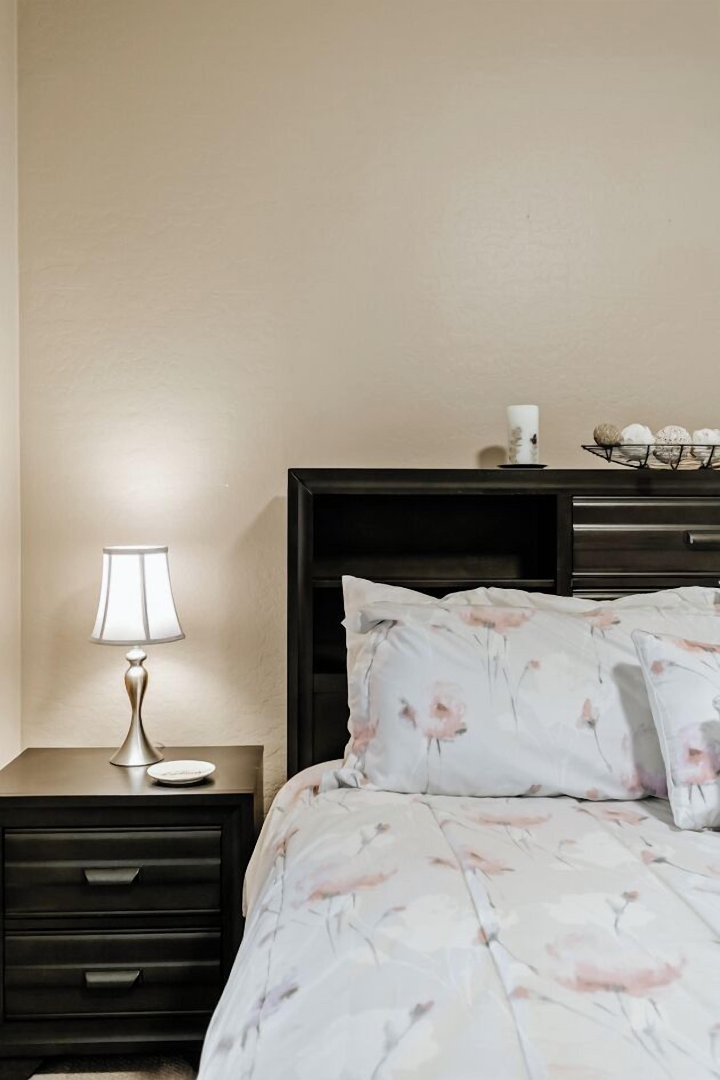 A neatly made bed with floral bedding, a bedside lamp, and a small bedside table with a lamp.