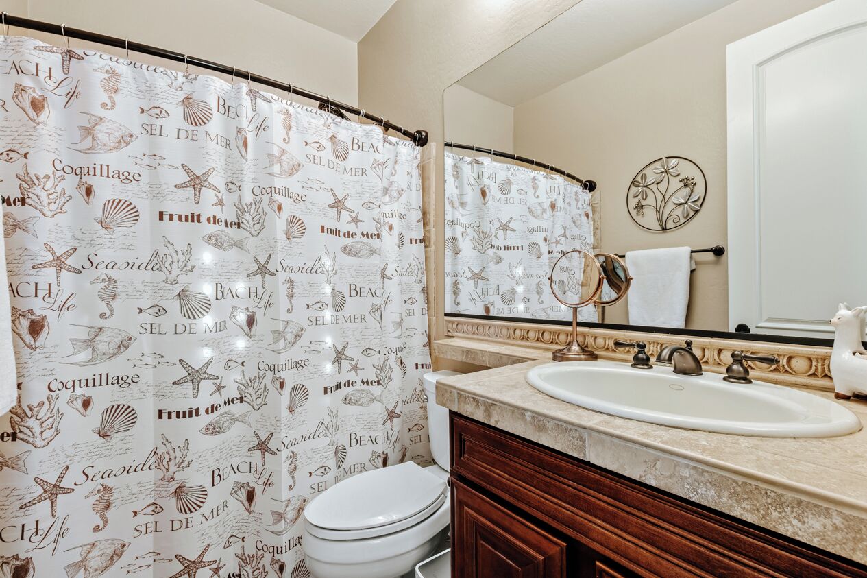 A bathroom with a shower curtain featuring sea life and beach-related text, a white sink, and a mirror above it.