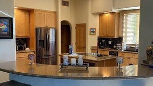 A modern kitchen with a central island, wooden cabinets, stainless steel appliances, and a large window providing natural light. - Casa Carefree 3 Bedroom Home by RedAwning (Carefree)