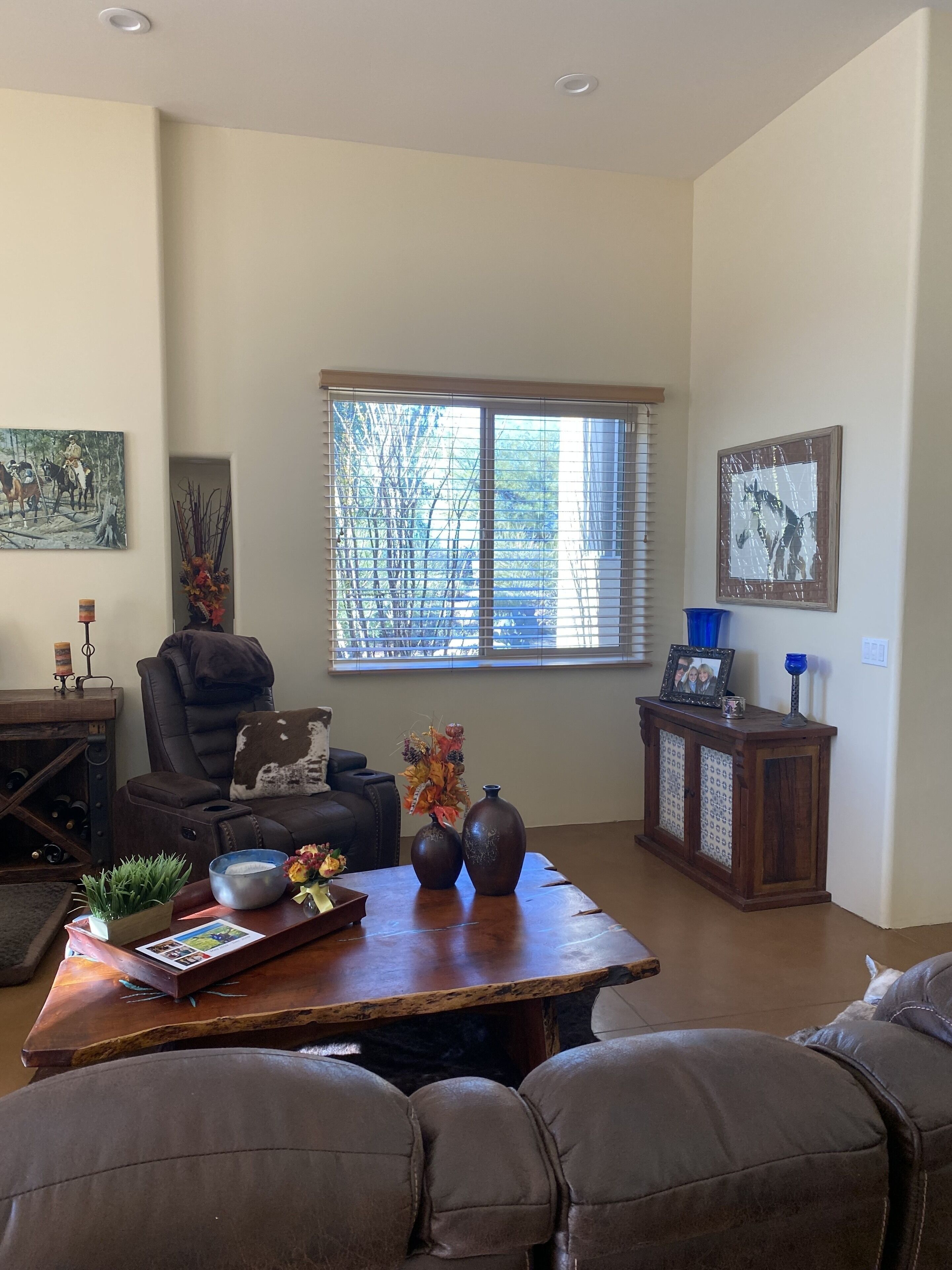 A living room with a leather sofa, a wooden coffee table, and a large window with blinds.
