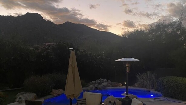 An outdoor patio with wicker furniture, a fire pit, and a pool with blue lighting. - Casa Carefree 3 Bedroom Home by RedAwning (Carefree)