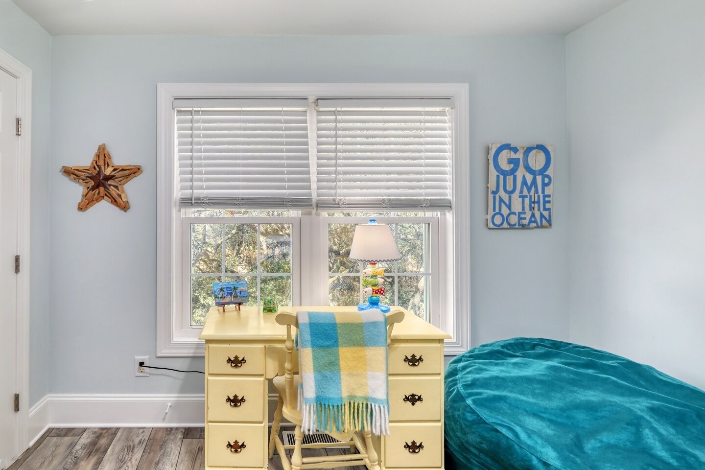 Un dormitorio con escritorio, una silla, una cama, una decoración de estrella de mar y un letrero que dice 'Go Jump in the Ocean'.