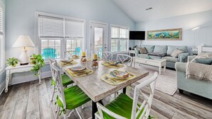 A spacious living room with a dining area, large windows, a ceiling fan, and a painting on the wall. - Beach Bliss: 4br Beach Access Kayak Wi-fi 4 Bedroom Home by RedAwning (Holly Ridge)