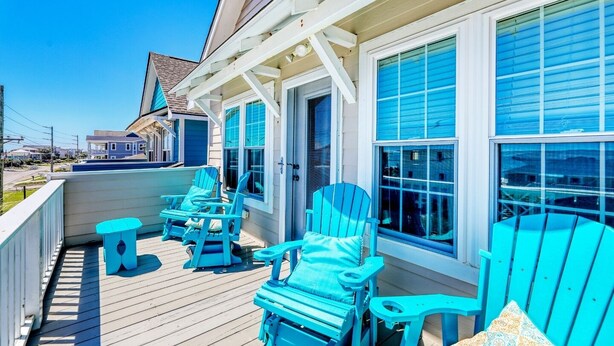 A wooden deck with blue Adirondack chairs and a small table, overlooking a residential area. - Beach Bliss: 4br Beach Access Kayak Wi-fi 4 Bedroom Home by RedAwning (Holly Ridge)