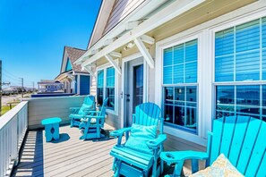 Terraza de madera con sillas Adirondack azules y una pequeña mesa, con vista a una zona residencial.