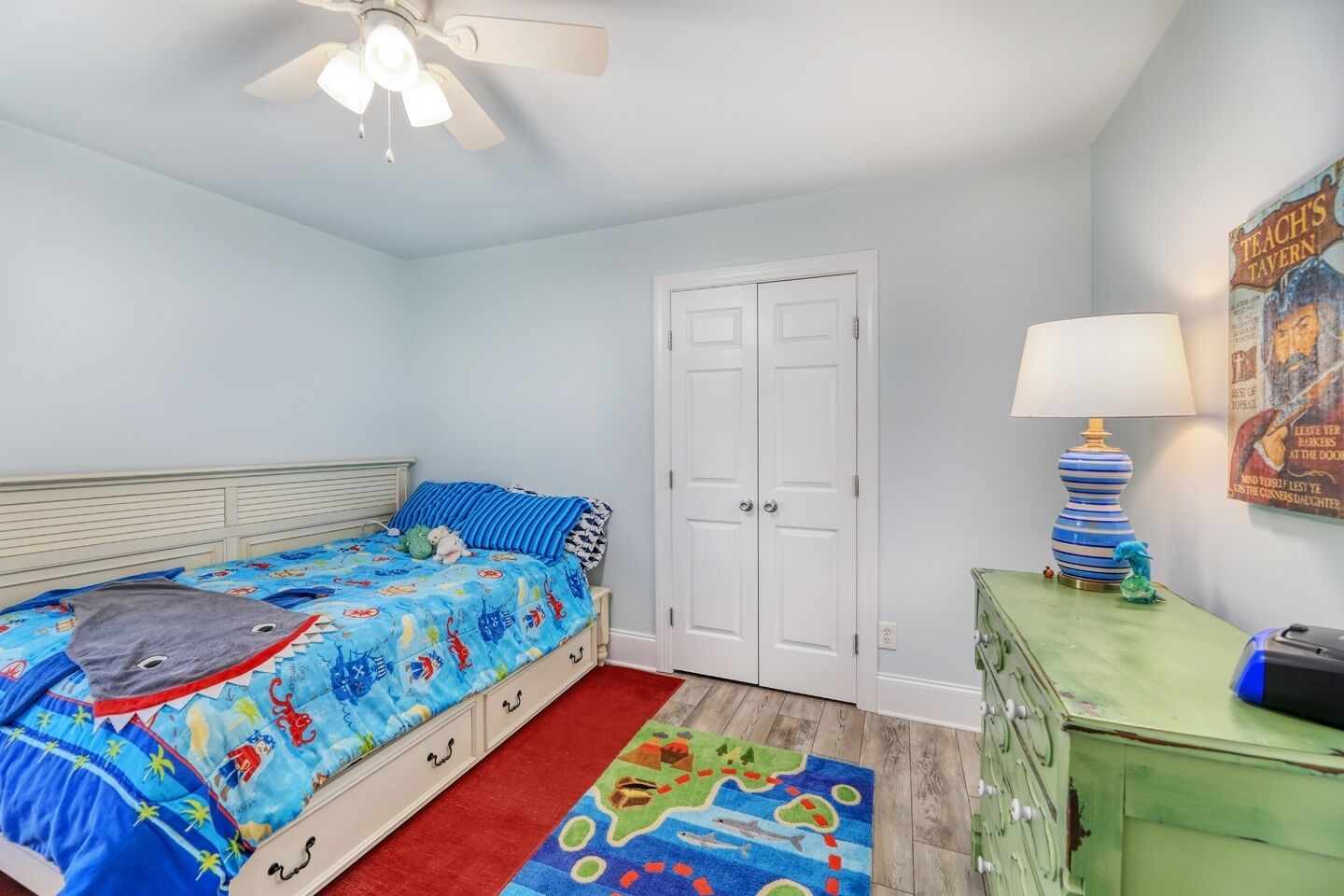 A bedroom with a bed, a dresser, a lamp, and a poster on the wall.