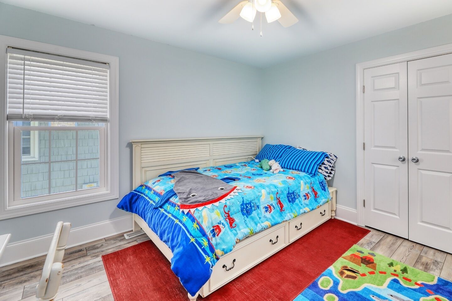 A bedroom with a bed, a window with blinds, a ceiling fan, and a door.