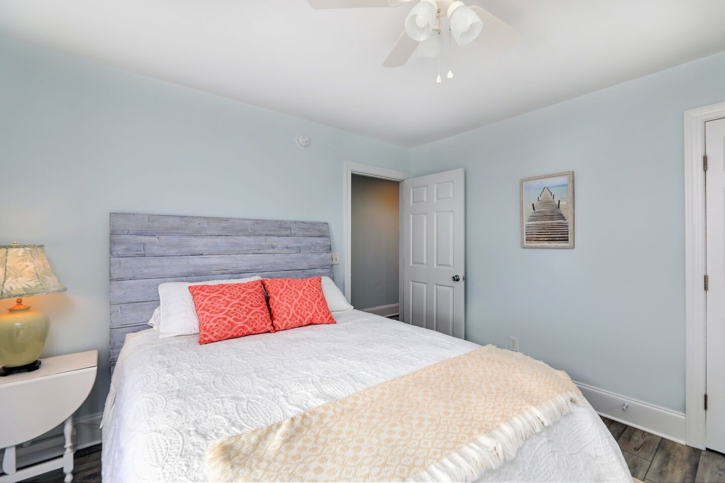 Une chambre à coucher comprenant un lit, une table de chevet, une lampe, un ventilateur de plafond et une porte.