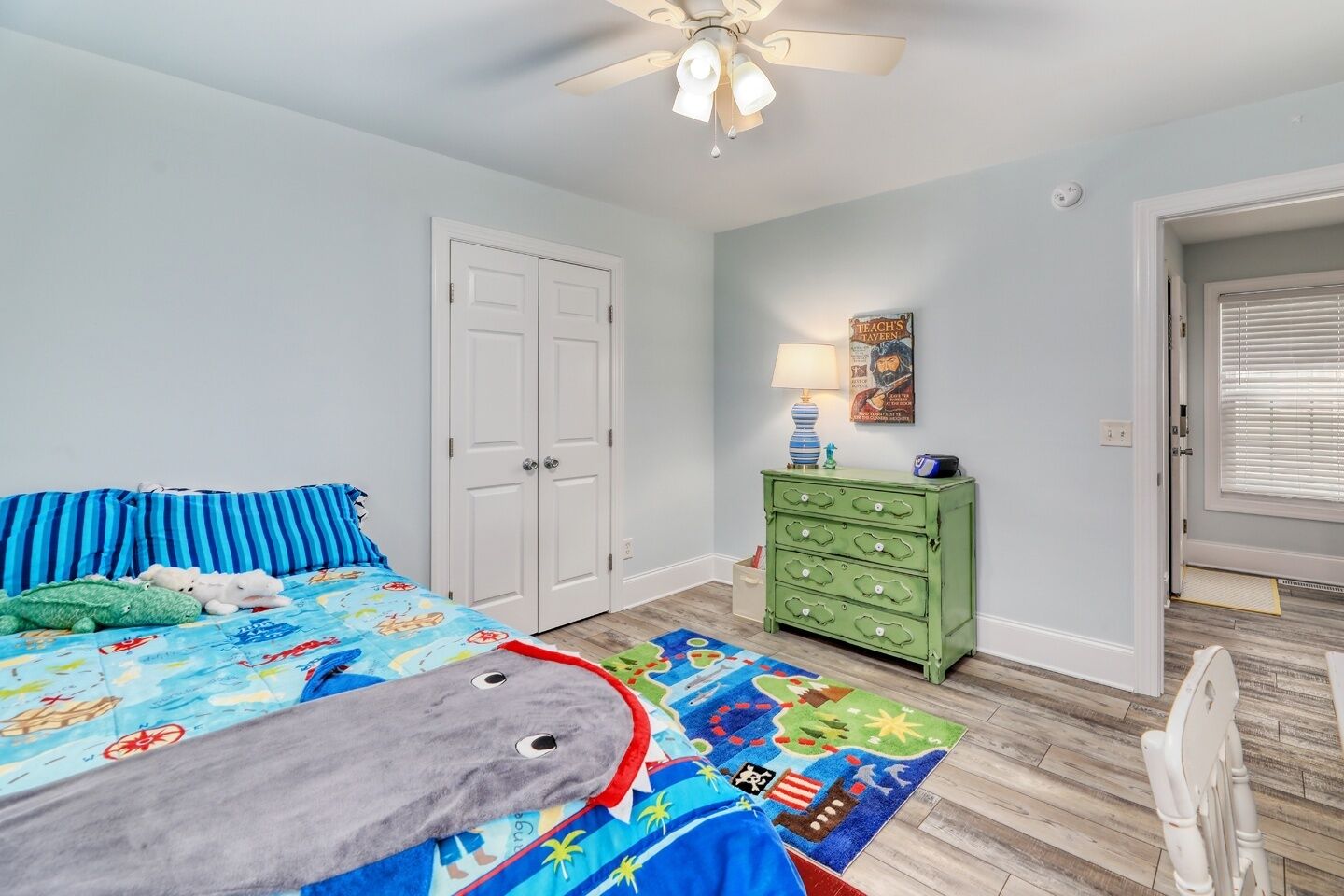A bedroom with a bed, a dresser, a lamp, and a ceiling fan.