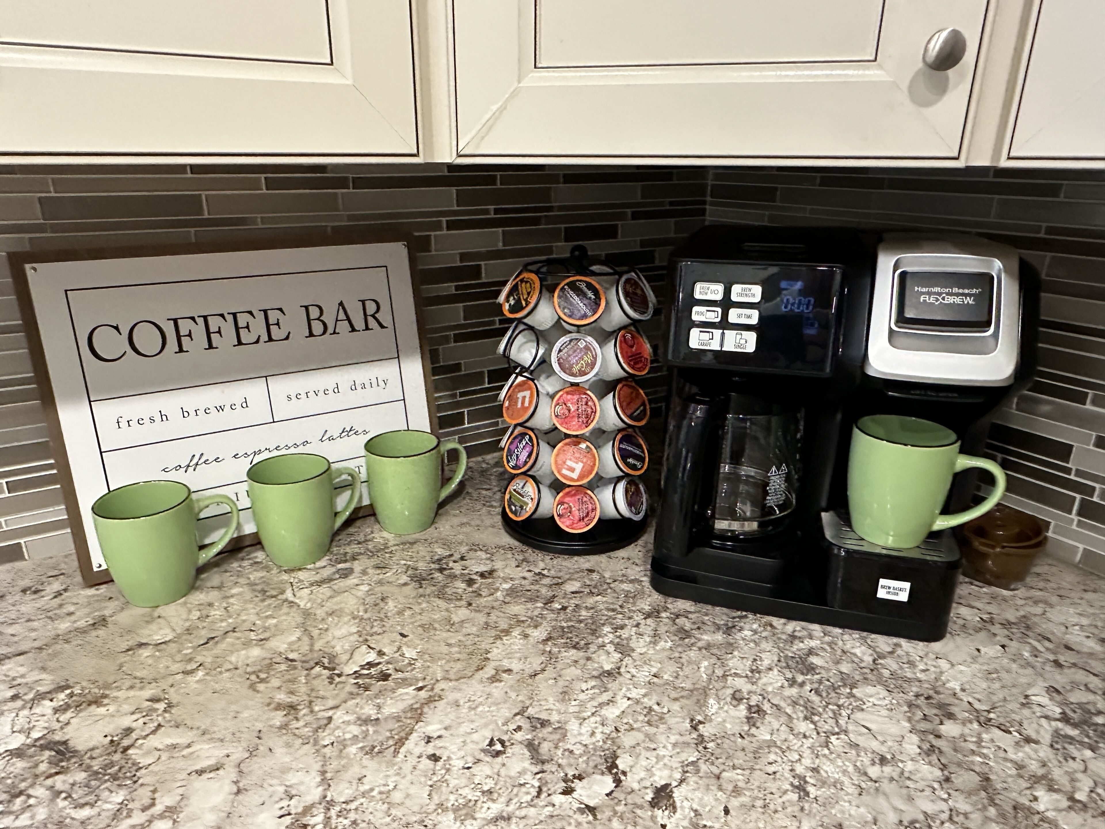 A kitchen counter with a coffee bar sign, a coffee machine, a mug rack, and two green mugs.