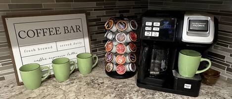 A kitchen counter with a coffee bar sign, a coffee machine, a mug rack, and two green mugs.