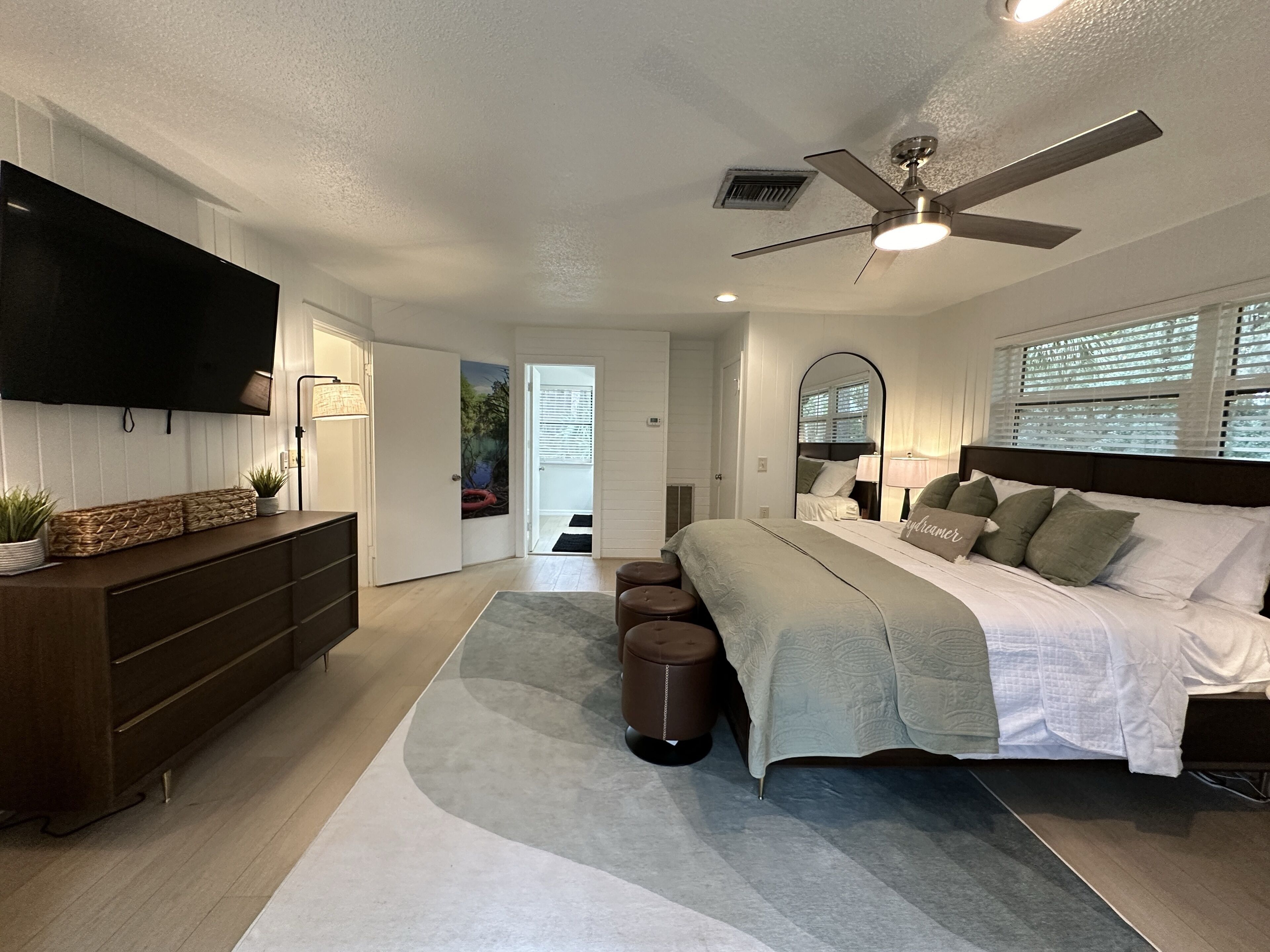Un dormitorio moderno con cama, ventilador de techo, televisión y cómoda.