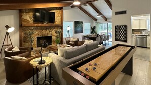 Amplia sala de estar con mesa de billar, chimenea de piedra, televisor y comedor con vistas al exterior.