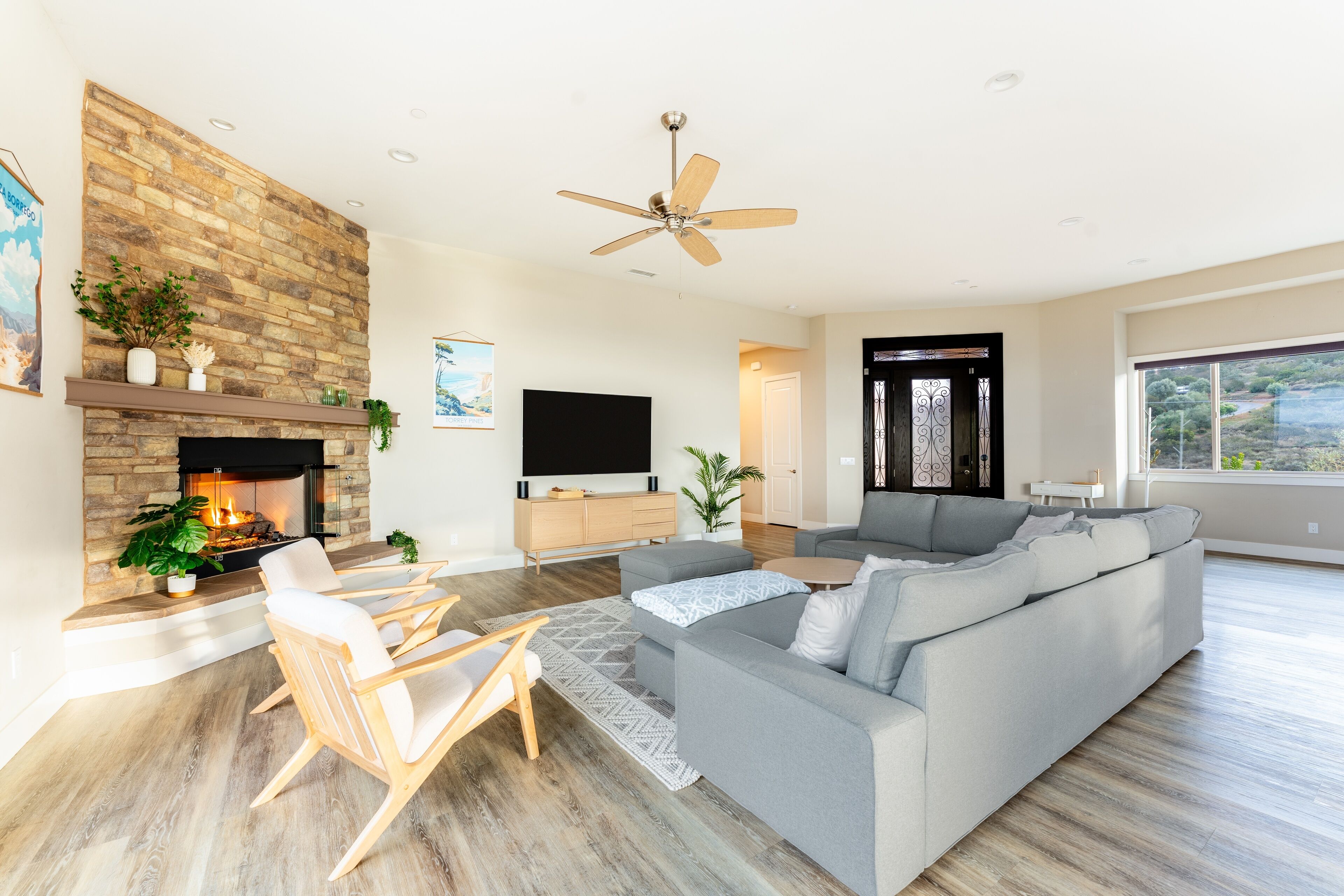 Un salon moderne avec une cheminée en pierre, un ventilateur de plafond, un canapé gris et un téléviseur à écran plat.