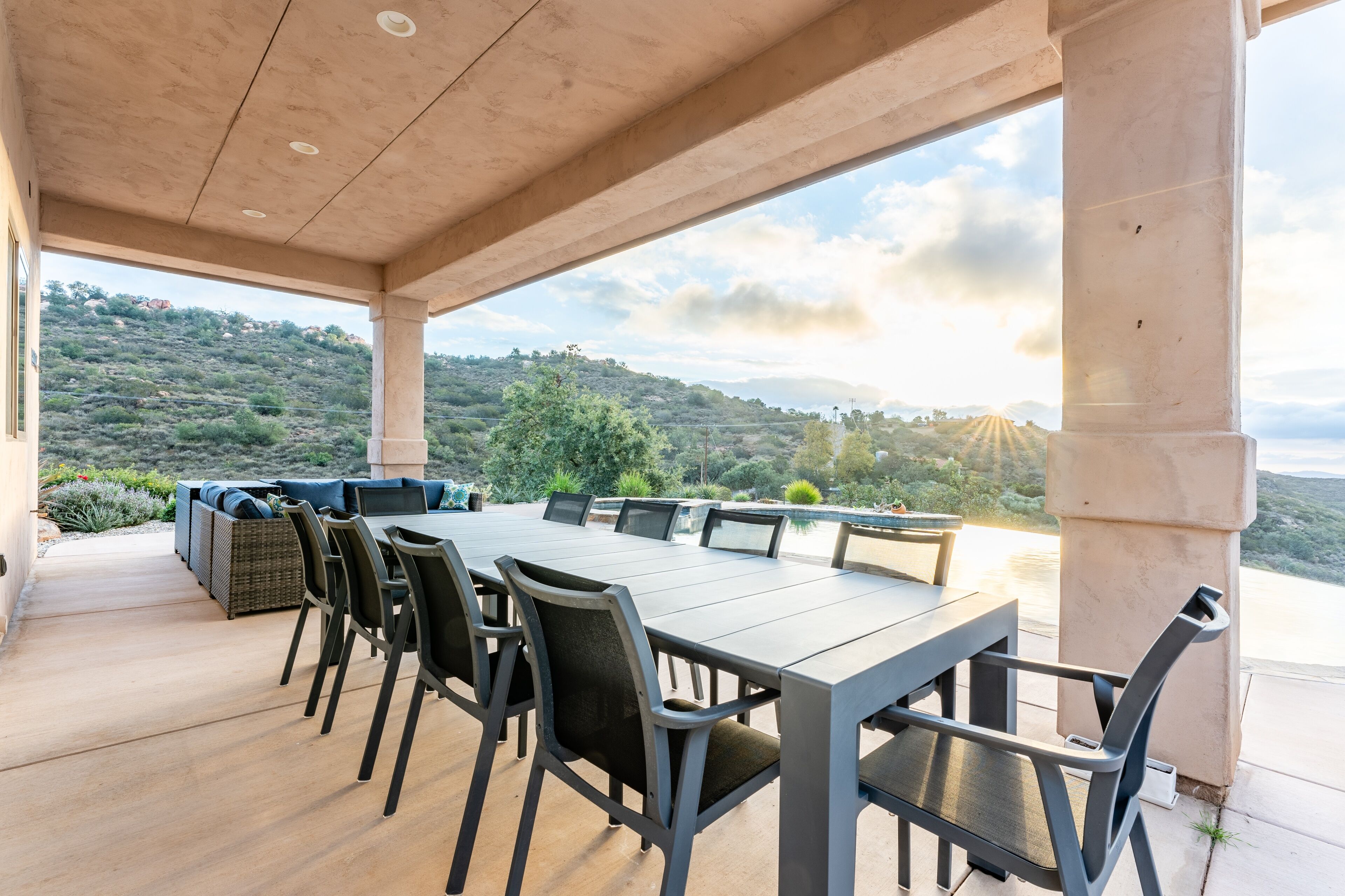 Une terrasse extérieure avec une longue table et des chaises, donnant sur un paysage vallonné.