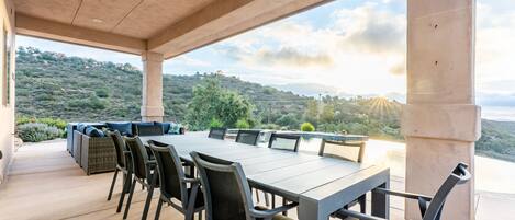 Une terrasse extérieure avec une longue table et des chaises, donnant sur un paysage vallonné.