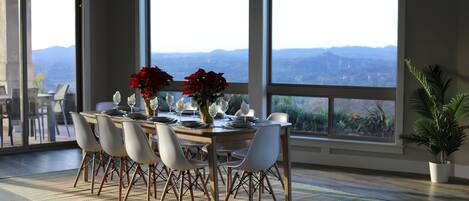 Comedor con mesa lista para seis personas, ventanas amplias y vista a las montañas.