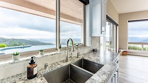 A kitchen with a large window, a sink, and a view of a lake and mountains. - San Diego Wine Country Pool, Views, 4BR (Ramona)