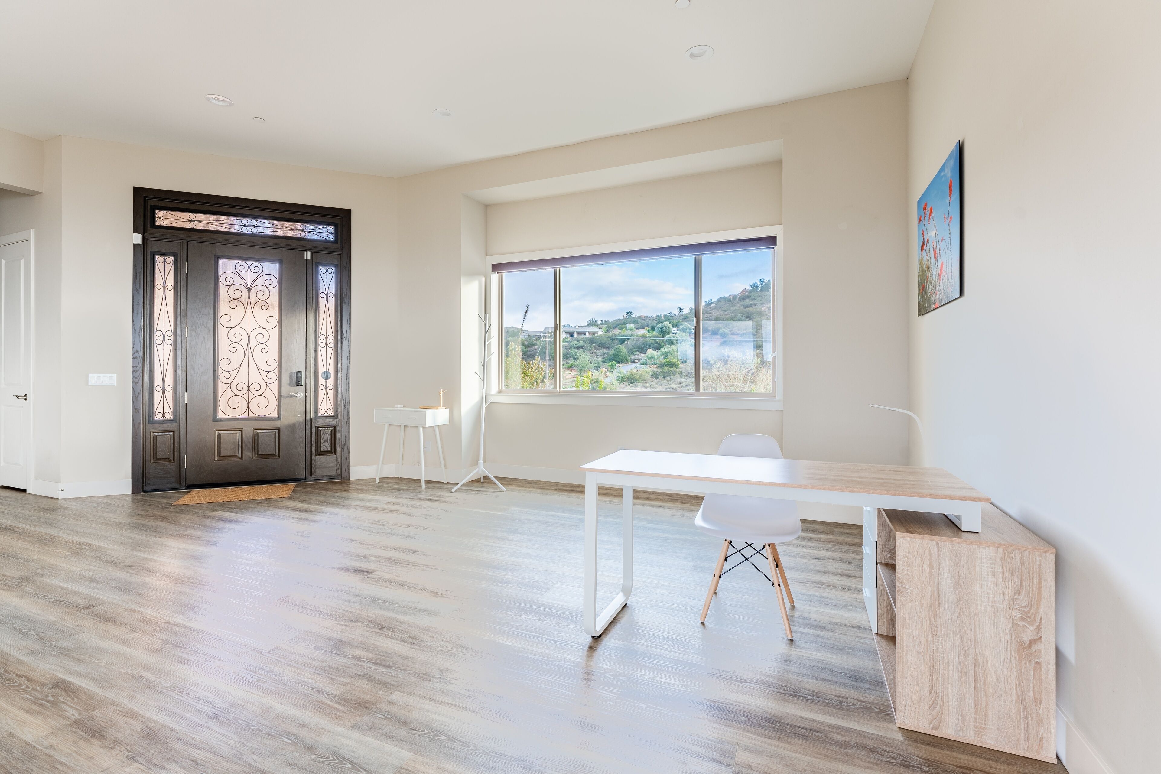 Een ruime kamer met een groot raam, een wit bureau en een deur met decoratieve glaspanelen.