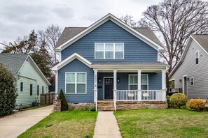 Stroll up the pathway to the charming front porch of this two-story home, marked by the address '207 E'.