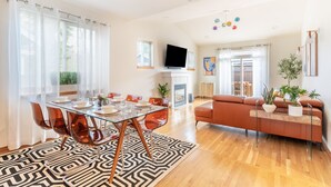 A modern living room with a glass dining table, orange sofa, and a fireplace.